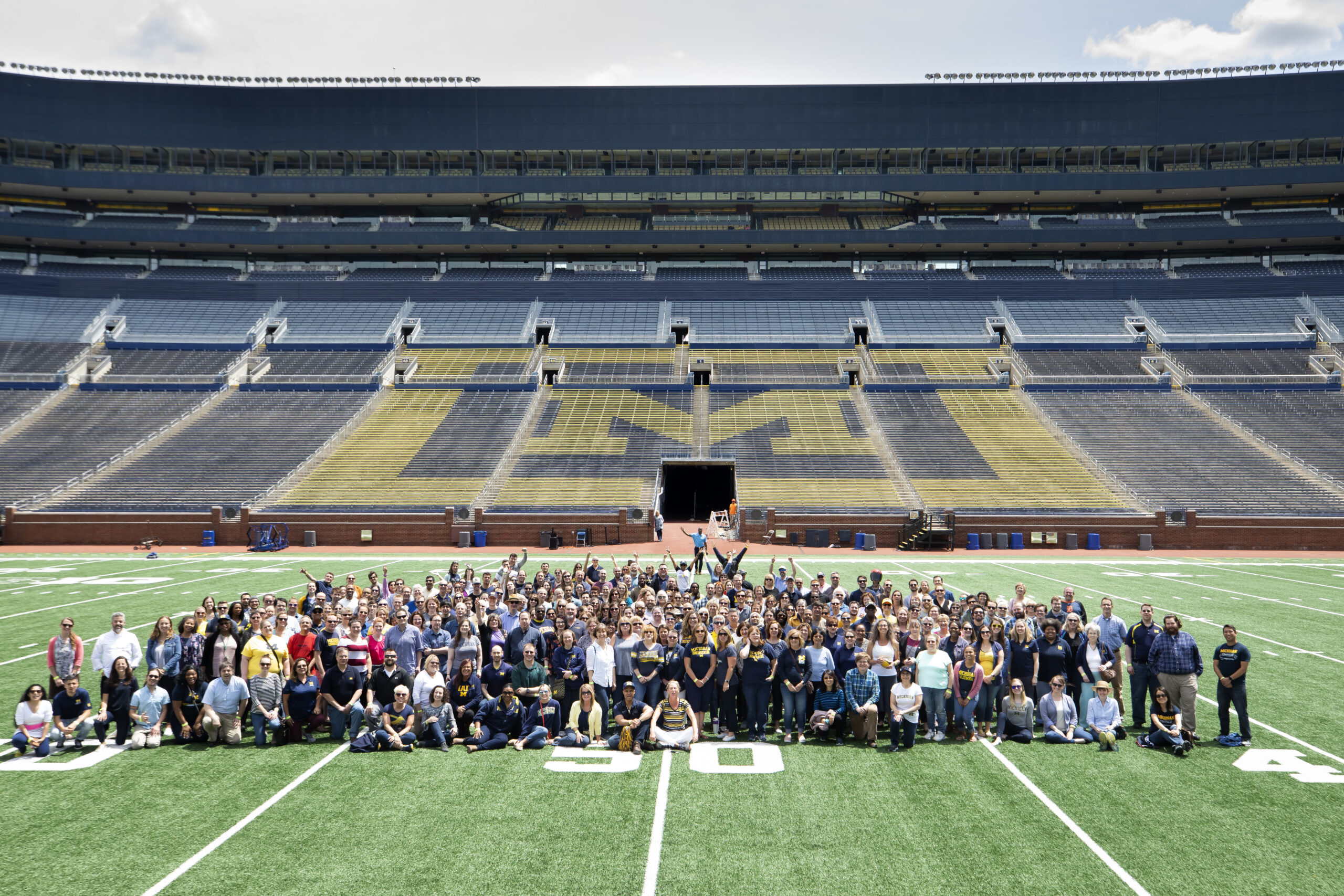 Large group of Michigan staff pose for photo on the Michigan football field