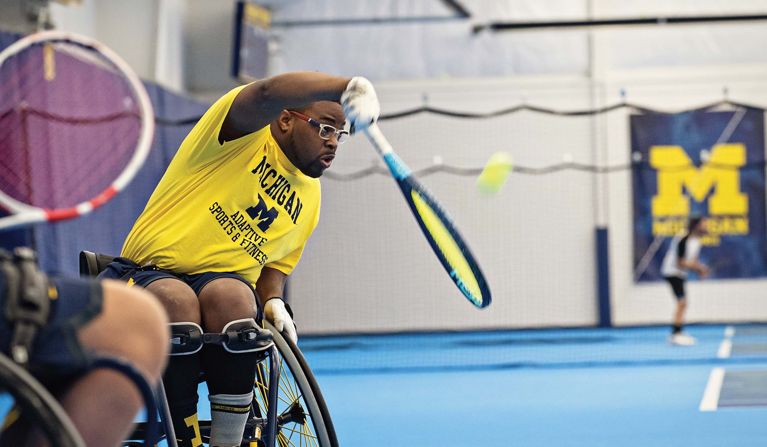 Tennis player in wheelchair hits tennis ball with racket