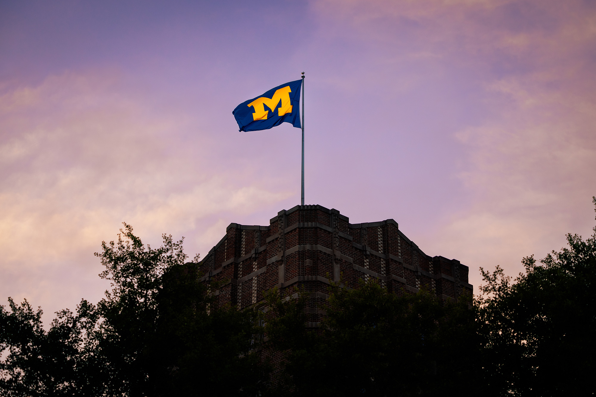 Block M flag flying over the Michigan Union at sunset.