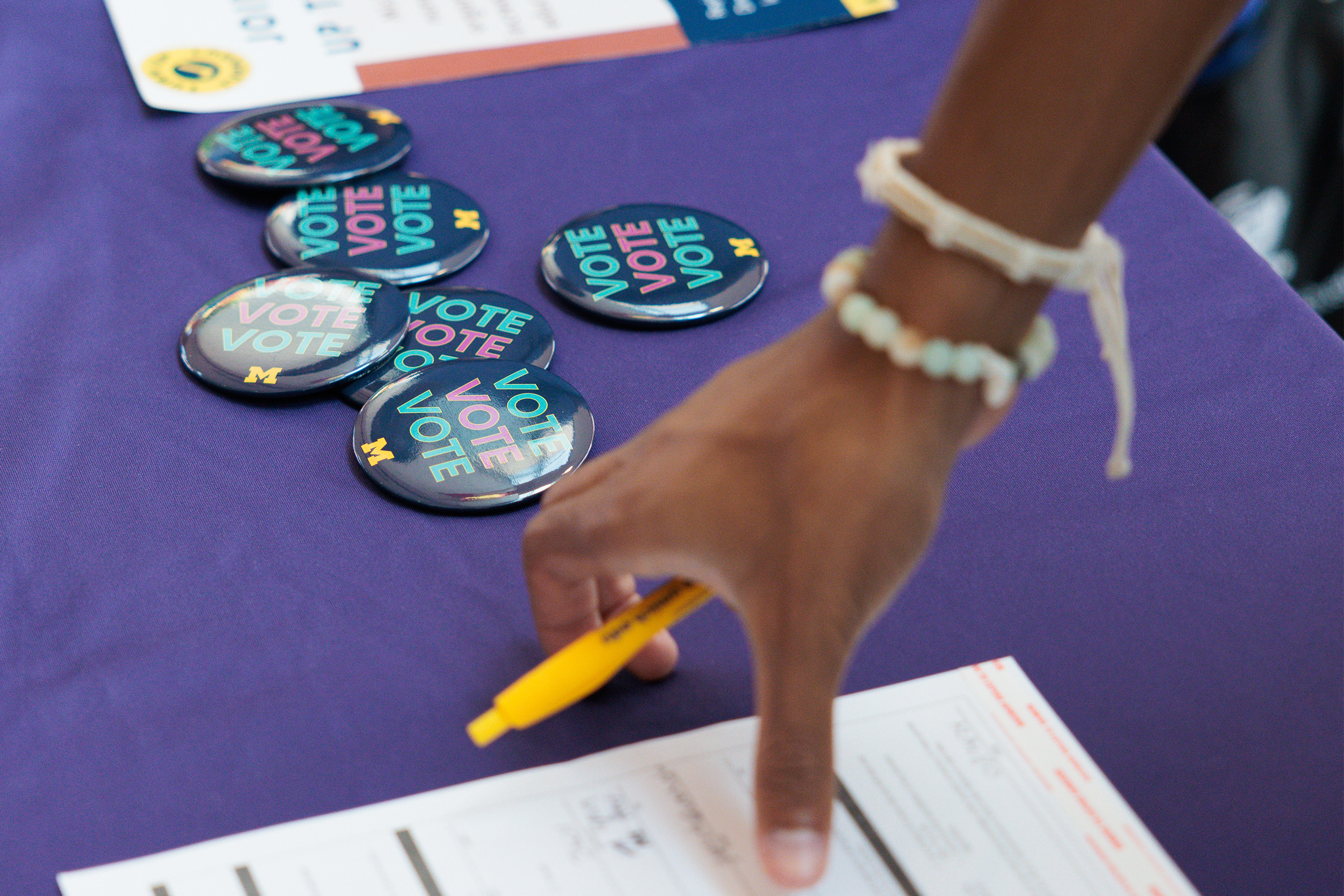 VOTE buttons on a purple table with hand holding a pencil and picking up a form